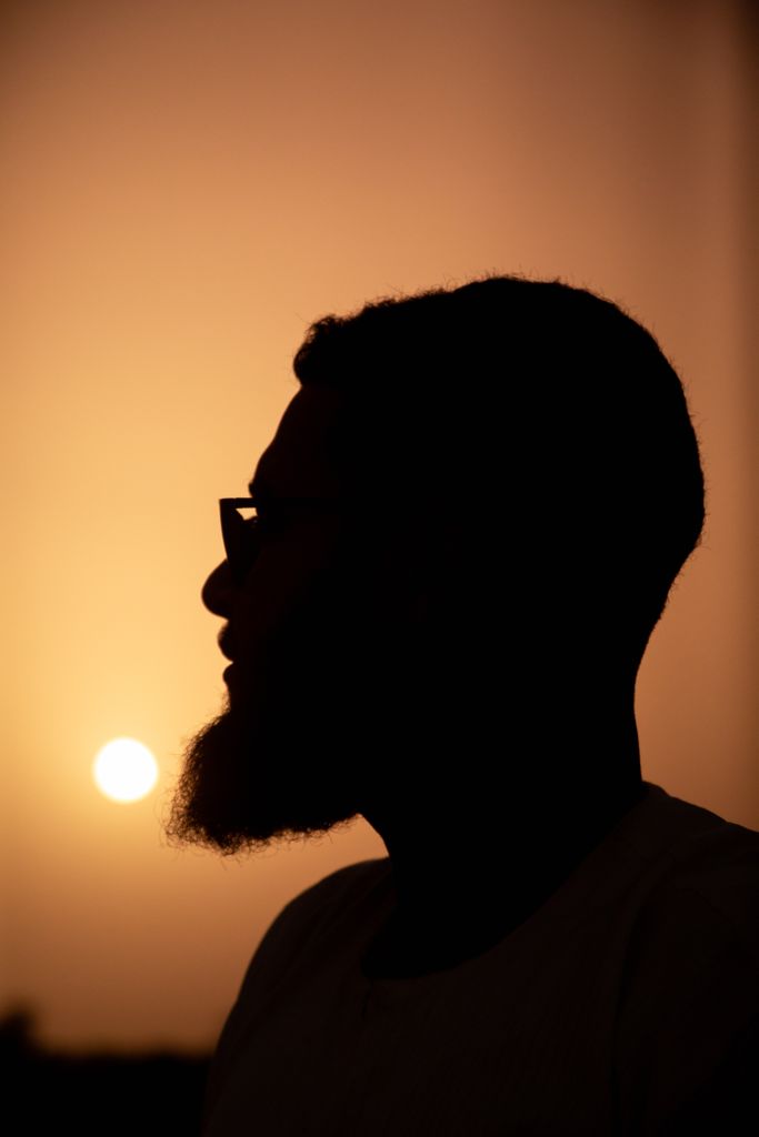Artistic silhouette of a man in profile against an orange sunset.