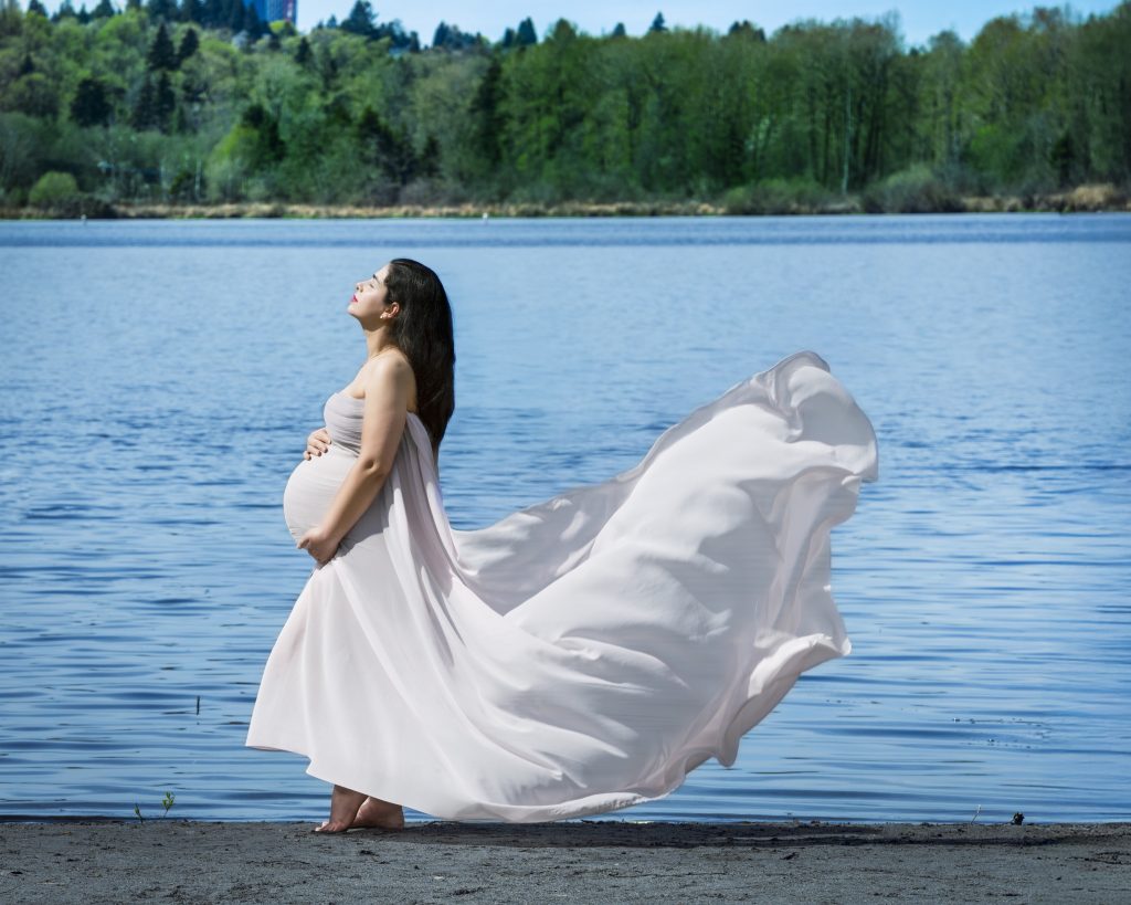 Pregnant mother in a flowing gown standing by a lake at golden hour, Nook Look outdoor maternity session, Coquitlam