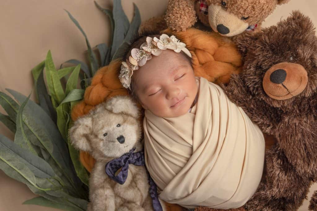 Newborn baby in a cream swaddle and floral headband, surrounded by teddy bears, Nook Look studio, Coquitlam