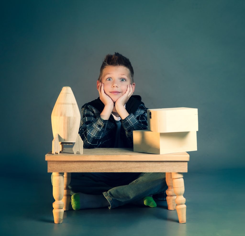 Young boy in a studio portrait session, resting his chin on his hands beside wooden toy props, Nook Look studio
